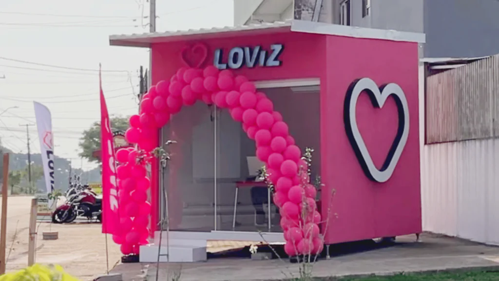 Loja quadrada rosa escrita LOViZ com arco de balões na porta em uma rua.